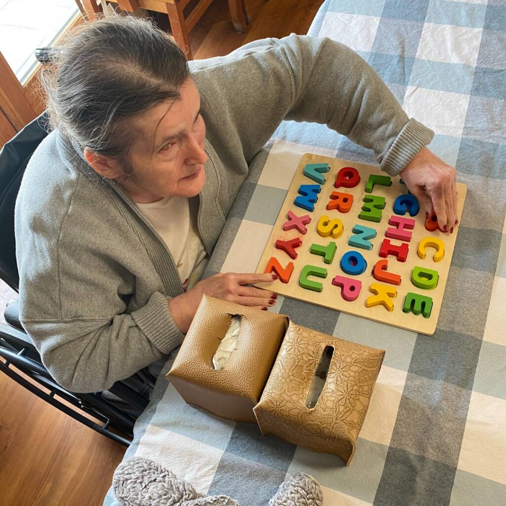 An older woman touches big and colorful alphabet blocks.