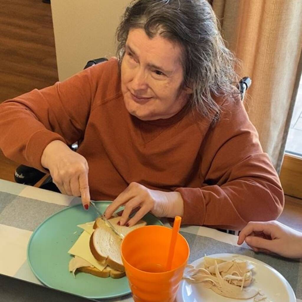 An older woman cuts a sandwich in half.