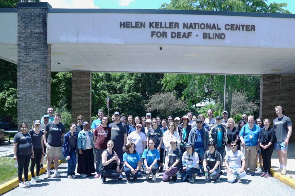 A group of Deloitte volunteers standing together with staff and participants at Helen Keller National Center.