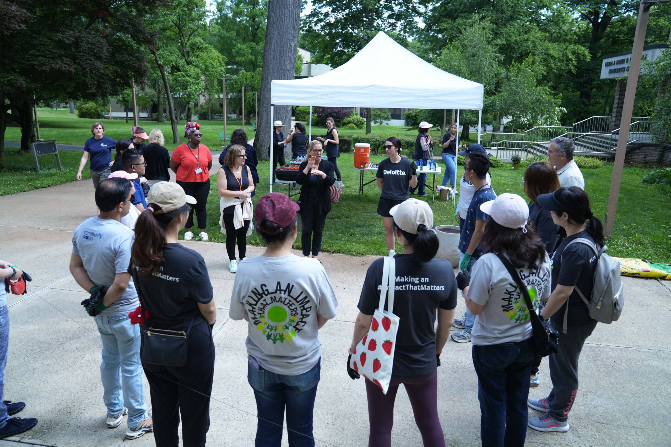 A group of Deloitte volunteers gathered outside in a circle and a female Interpreter is signing.