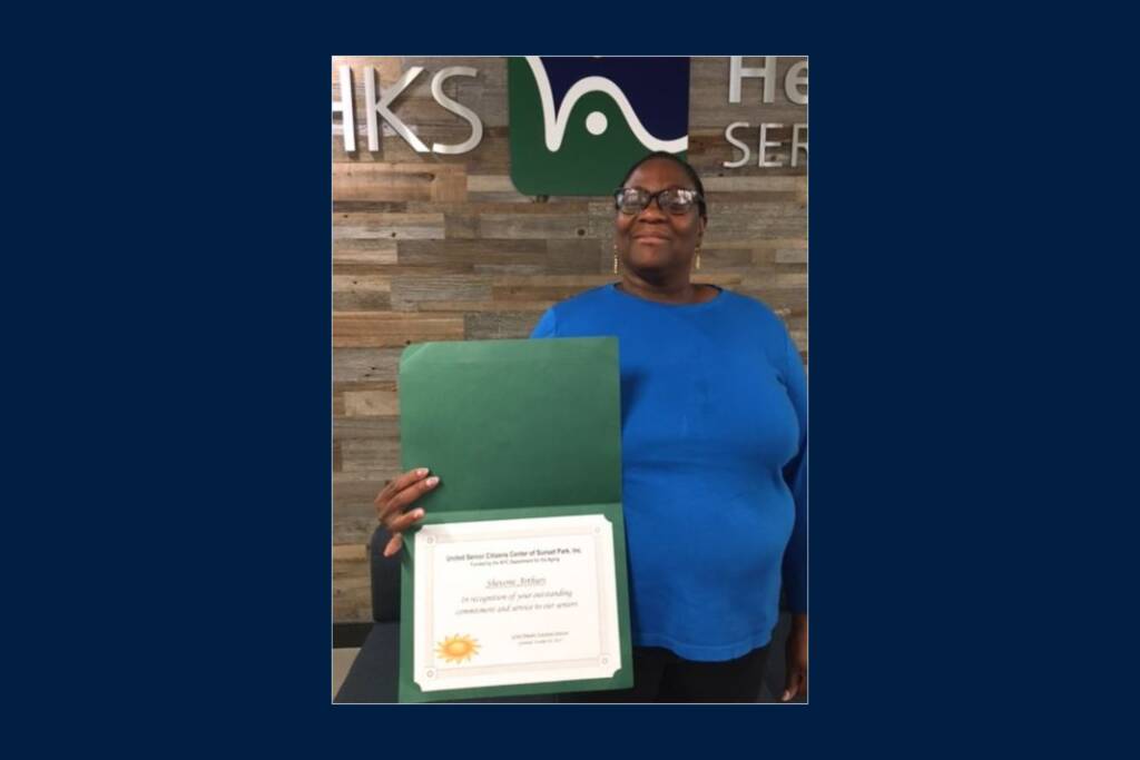 A woman smiling and holding her recognition award that notes her outstanding commitment and service to seniors at a senior center.