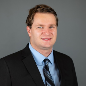 A headshot of a man in a suit smiling into the camera.