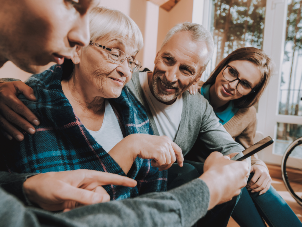 An older woman looking at a phone that a man is holding in front of her. The older woman is also next to an older man and another woman.