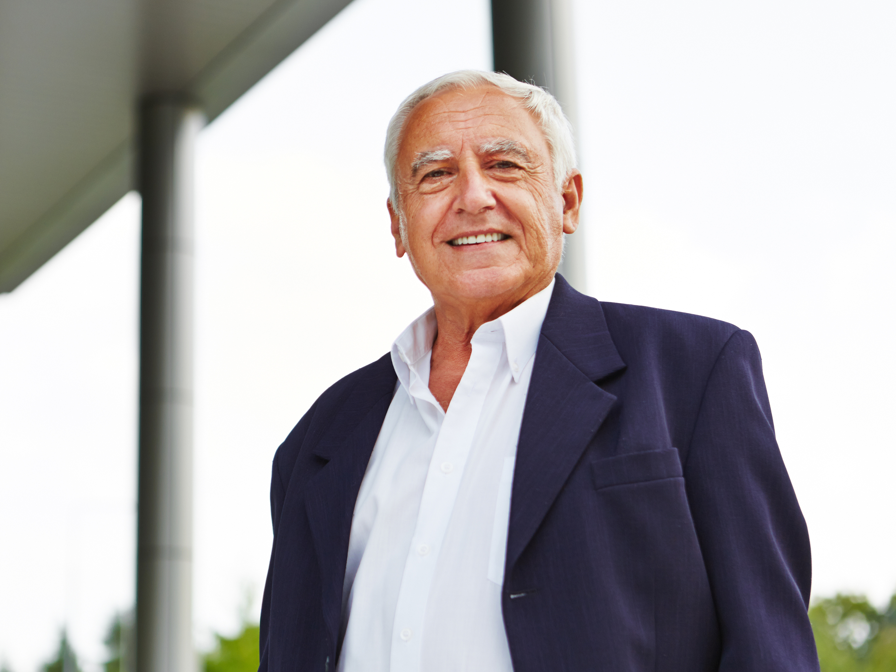 A headshot of a smiling older man wearing a collared shirt and a suit jacket.