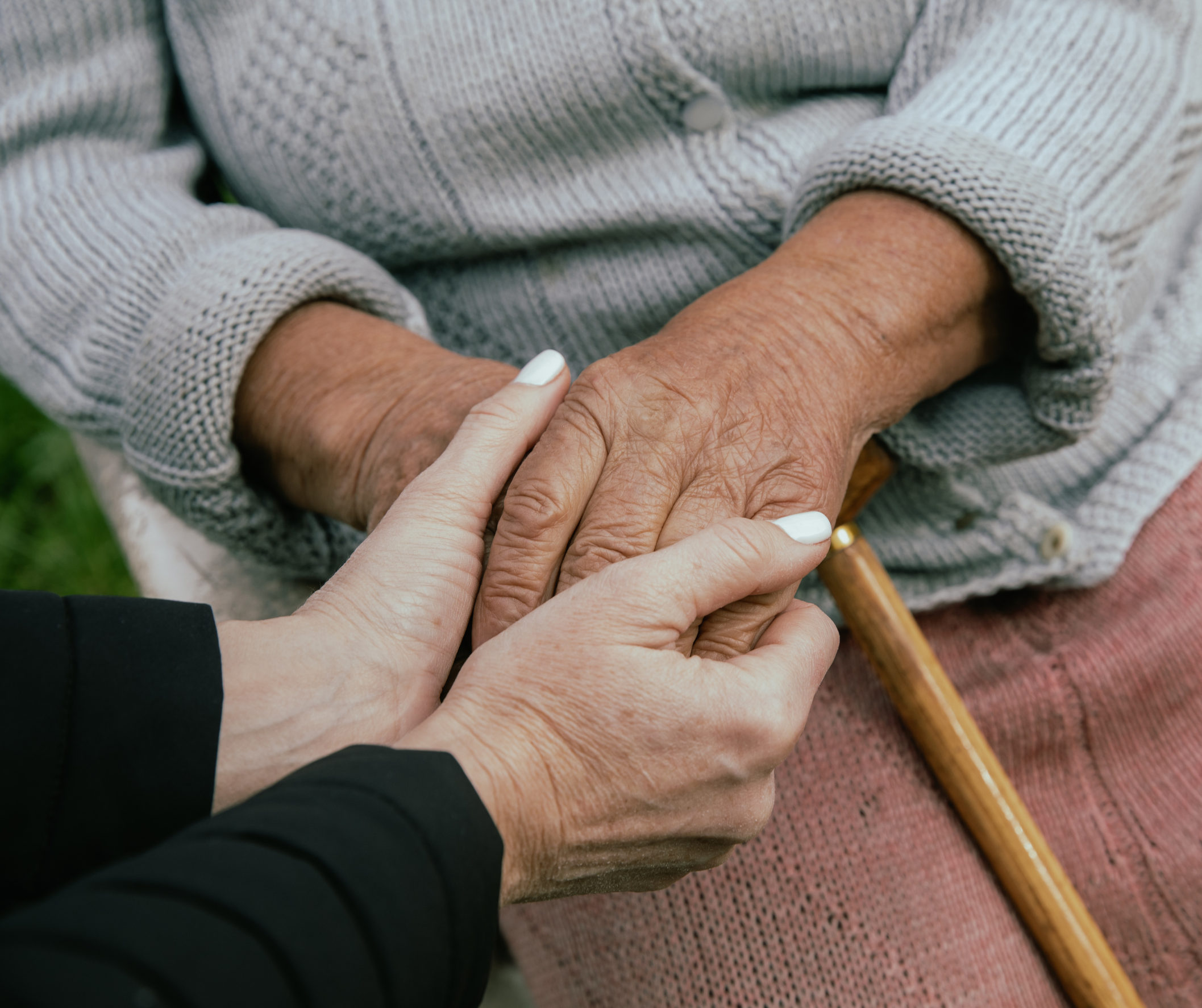 A close up of a person's hands holding an older adult's hands.