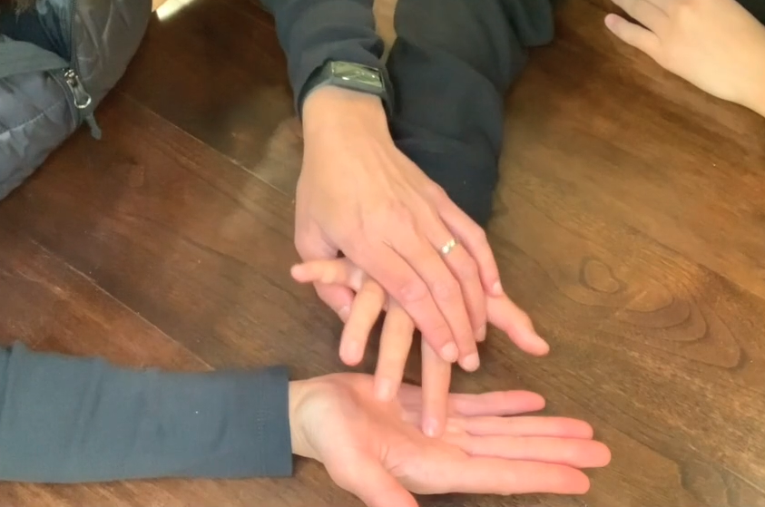 A close up of hands. One person presses the fingers of someone else's hand into their own open palm.