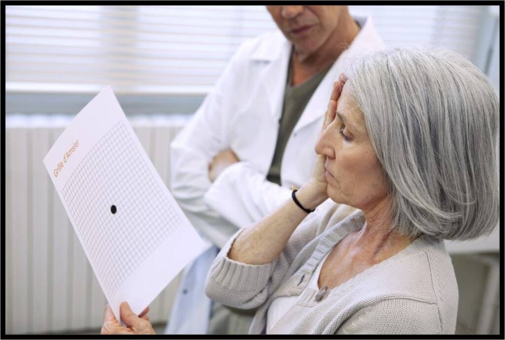 A woman with gray hair looks at a sheet of paper with lines and a circle as she covers her right eye with her right hand. Beside her there is a person wearing a white lab coat, also looking at the paper.