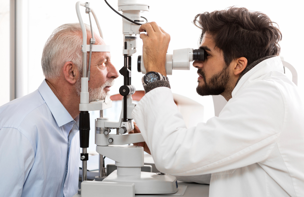 An older man is seated across from a doctor who is examining his eyes.