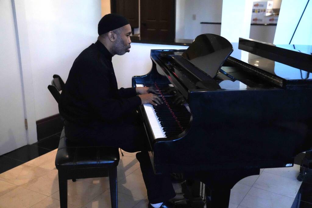 Side view of a man playing a baby grand piano.