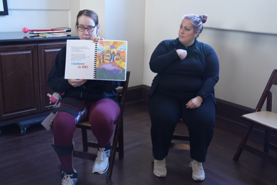 A female adult reading a book alongside an interpreter who is signing in ASL