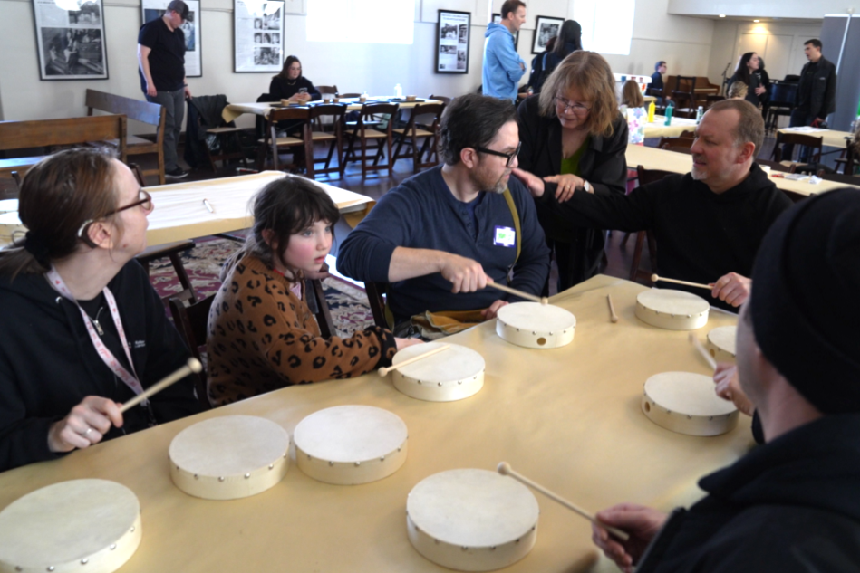 A group of adults and children participate in a haptics drum circle.